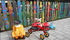 Fahrzeuge - Das Bild zeigt Kinderfahrzeuge vor einem bunt bemalten Zaun